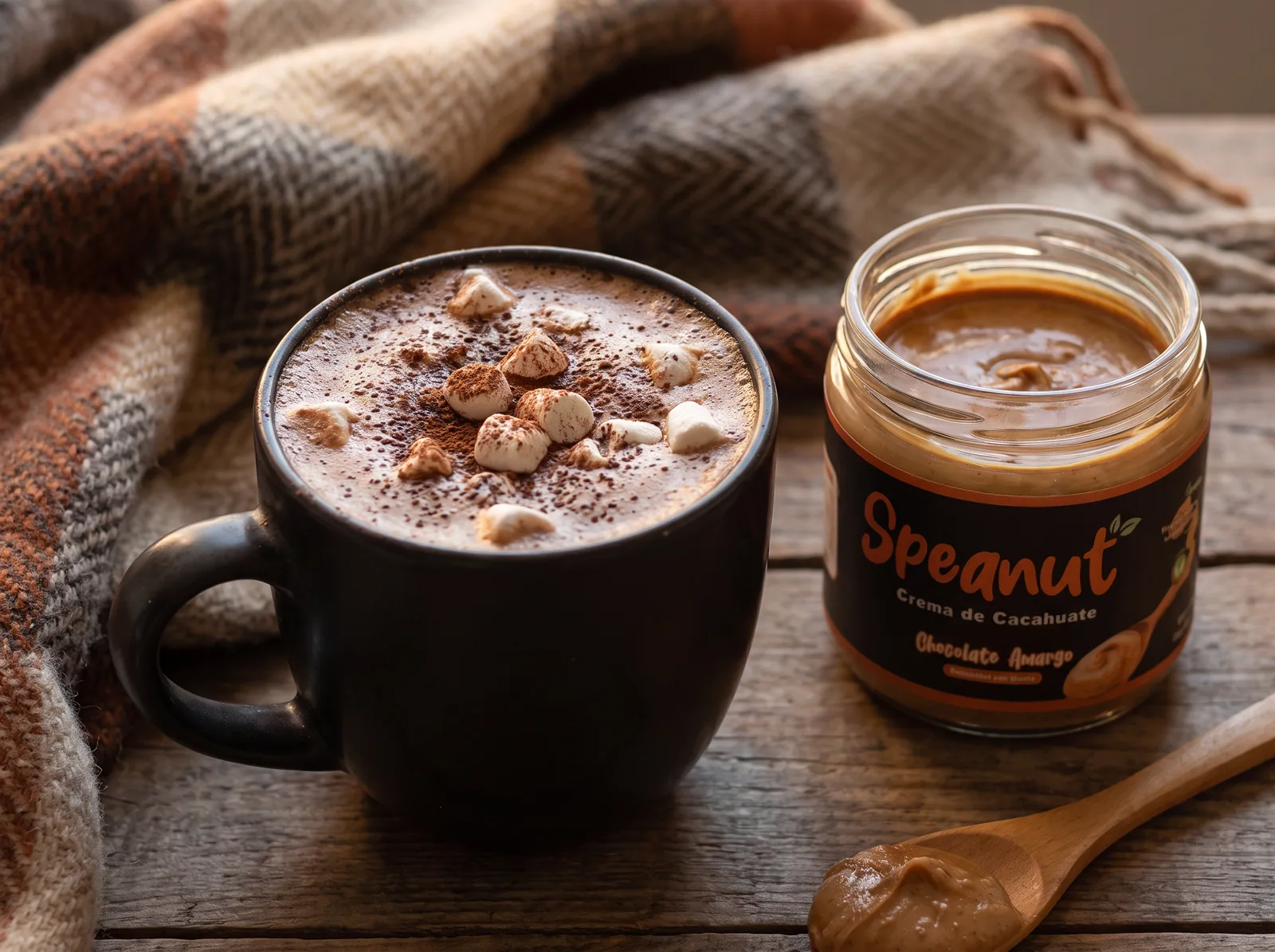 Taza negra con chocolate caliente cubierto de bombones pequeños y cacao espolvoreado, sobre una mesa de madera oscura